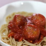 Vegan gehaktballen in tomatensaus geserveerd met spaghetti op een bord.