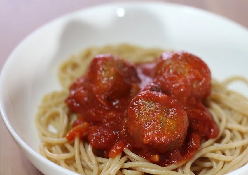 Vegan gehaktballen in tomatensaus geserveerd met spaghetti op een bord.