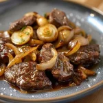 Rundvlees gesauteerd met uien en zoetzure saus op een bord.